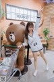 A woman pushing a shopping cart next to a giant teddy bear.