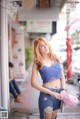 A woman in a blue top and denim shorts standing on a sidewalk.