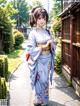 A woman in a blue kimono standing on a sidewalk.