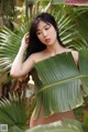 A woman in a bikini posing in front of a palm tree.