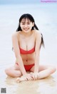 A woman in a red bikini sitting on the beach.