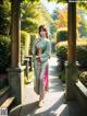 A woman in a green kimono standing in a garden.