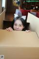 A young girl peeking out of a cardboard box.