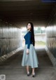 A woman in a blue top and a gray skirt standing in a tunnel.