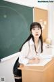 A woman sitting at a desk in front of a blackboard.