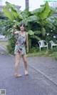 A woman standing in the middle of a street next to a banana tree.