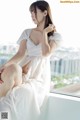 A woman in a white dress sitting on a window sill.