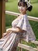 A woman in a floral dress sitting on a wooden railing.