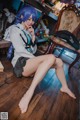 A woman with blue hair sitting on a wooden floor.